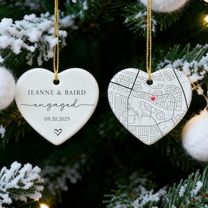 May include: Two heart-shaped Christmas ornaments hanging on a tree. One ornament has the text "JEANNE & BAIRD engaged 09.20.2025" and a heart symbol. The other ornament features a map design with a red marker.