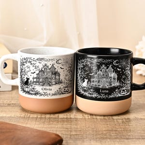 May include: Two ceramic mugs with a terracotta base. The left mug is white with black ink illustrations of a haunted house, ghosts, a cat, and pumpkins, featuring the name Olivia. The right mug is black with white ink illustrations and the name Luna.