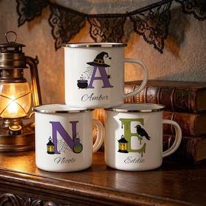 Puede incluir: Tres tazas de esmalte blanco con bordes plateados, cada una con una letra grande y gráficos temáticos de Halloween. Las tazas están personalizadas con los nombres Amber, Nicole y Eddie en letra cursiva, mostrando ilustraciones de un sombrero de bruja, telaraña, caldero, linterna, frasco de poción y un cuervo negro.