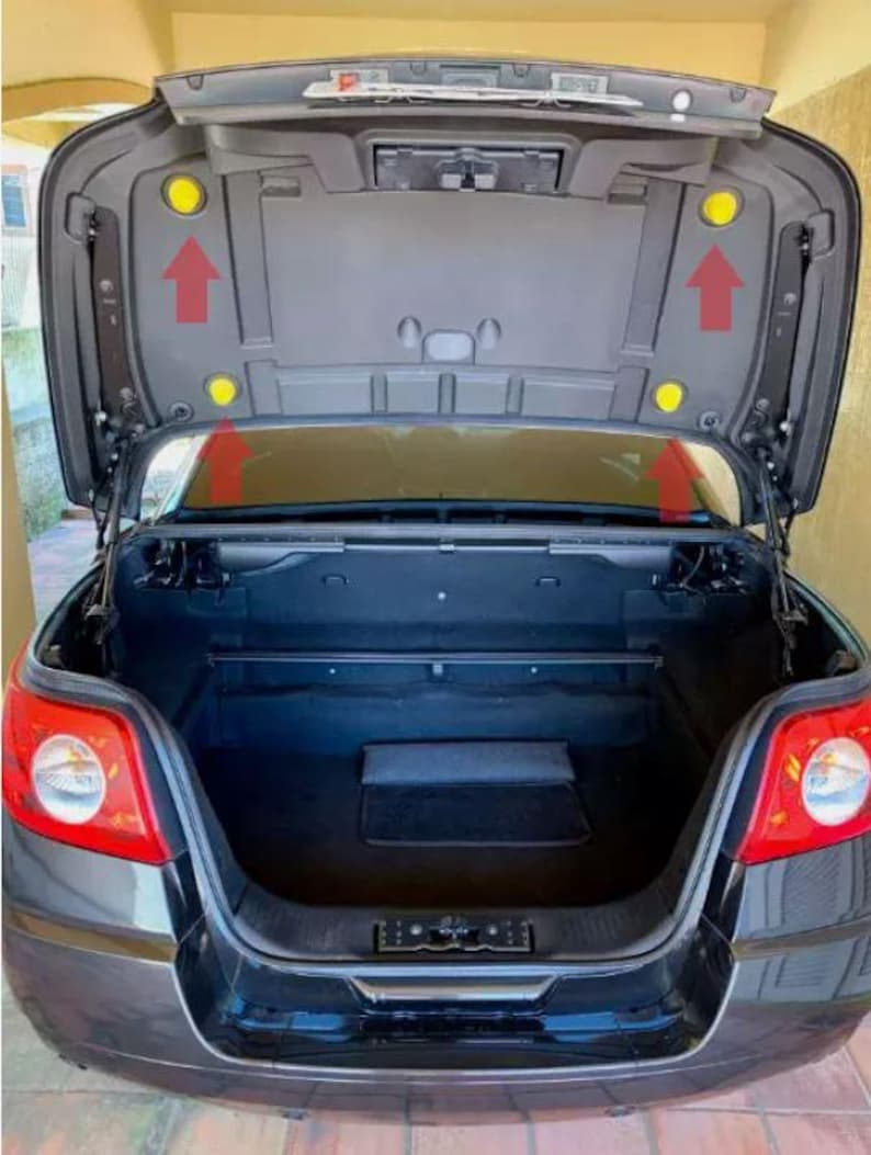 May include: A black convertible car with the trunk open. The trunk is empty and has a black mat on the floor. There are two yellow plastic caps on the trunk lid.