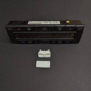 Può includere: Pannello di controllo dell'auto in plastica nera con pulsanti per il controllo del clima, tra cui AUTO, EC, REST e un pulsante con un'icona di un'auto. Il pannello ha il testo "MERCEDES-BENZ" e "GKR 140 010 177" stampato su di esso. Ci sono due connettori in plastica bianca accanto al pannello.