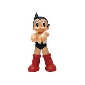 May include: Astro Boy sticker. The sticker features a cartoon figure with black hair, a tan face, and red boots. The character is wearing black shorts and a green belt. The figure is pointing with both hands.