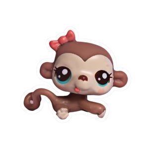 Puede incluir: Figura de mono marrón y beige con un lazo rojo en la cabeza. El mono tiene ojos grandes con detalles turquesa y una pequeña lengua rosa. Es un juguete coleccionable de estilo caricatura.