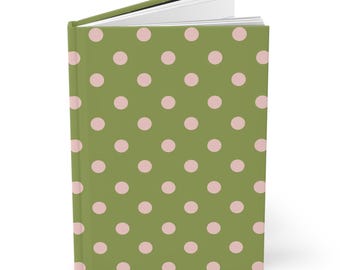 May include: A hardcover journal with a green cover featuring a pattern of pink polka dots. The journal is open, revealing the blank white pages inside. The spine is visible, and the book is set against a white background.
