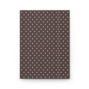 May include: A brown notebook featuring a pattern of small, evenly spaced pink polka dots. The cover is rectangular and appears to be made of a smooth material. The design is simple and classic.