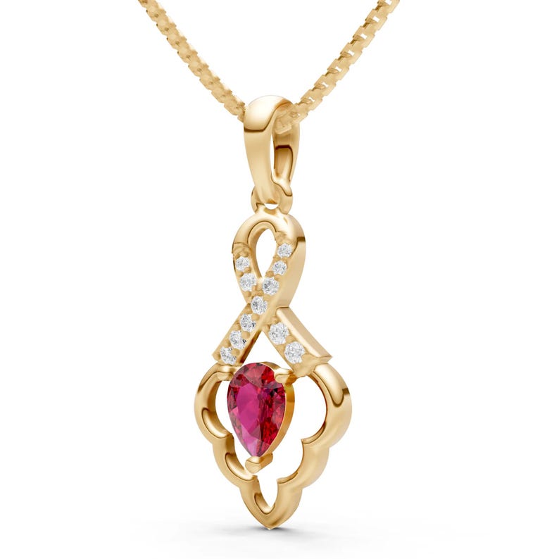 May include: A gold pendant necklace featuring a pear-shaped, deep red gemstone. The pendant has a decorative design with small, clear gemstones and is suspended from a delicate gold chain.