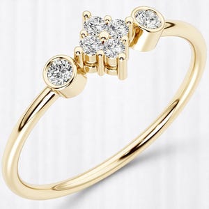May include: A delicate gold ring featuring a cluster of five small diamonds at the center, with a single diamond set in a bezel on each side. The ring has a smooth, polished band.