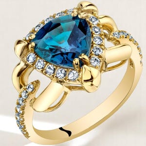 May include: A gold ring with a triangular teal gemstone, encircled by small, clear gemstones. The ring's design includes additional clear gemstones along the band, with a decorative gold setting.