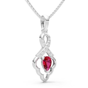May include: A silver pendant necklace featuring a teardrop-shaped, vibrant red gemstone. The pendant has a decorative, openwork design with small, clear accent stones. The necklace chain is a delicate, silver cable.
