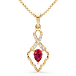 May include: A gold-colored pendant necklace featuring a pear-shaped, deep red gemstone at the bottom. The pendant has a decorative openwork design with small, clear gemstones and is suspended from a delicate gold chain.