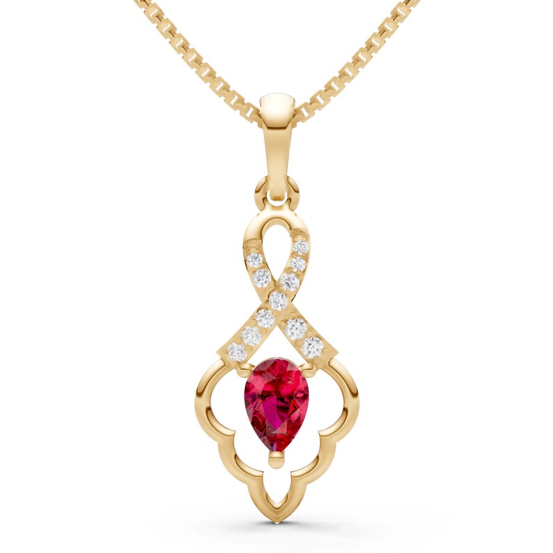 May include: A gold-colored pendant necklace featuring a pear-shaped, deep red gemstone at the bottom. The pendant has a decorative openwork design with small, clear gemstones and is suspended from a delicate gold chain.