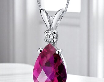 May include: A silver pendant necklace featuring a pear-shaped, faceted, deep pink gemstone. A small, round, clear gemstone is set above the larger stone. The pendant hangs from a delicate silver chain. The jewelry is displayed against a soft, blurred background.