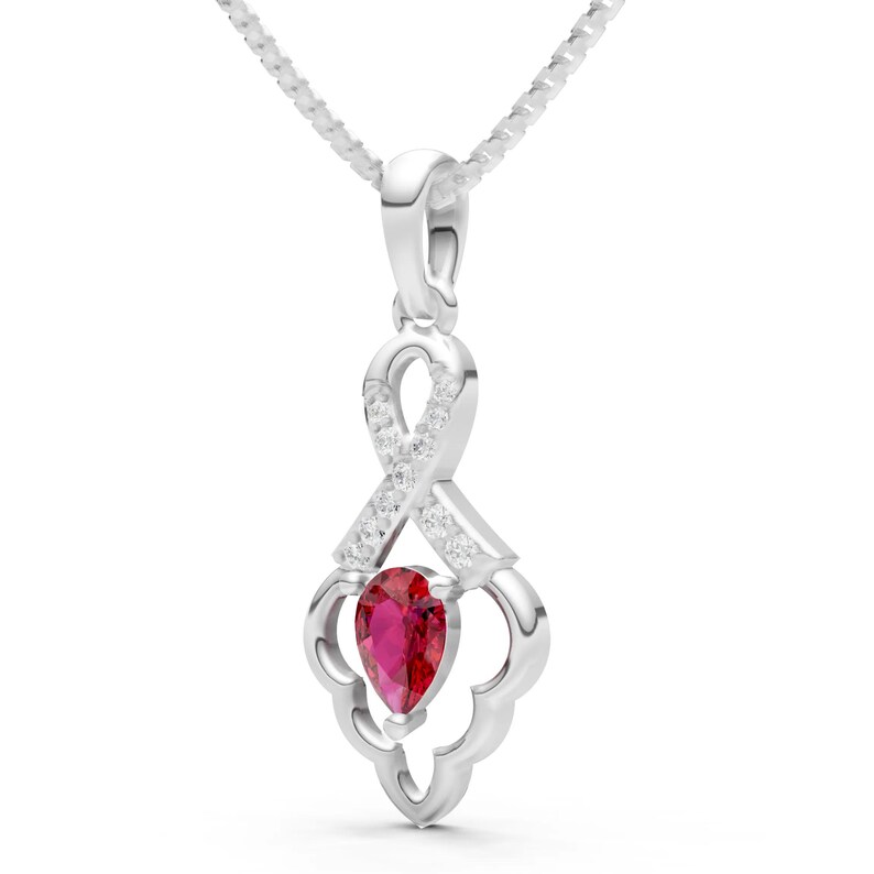 May include: A silver pendant necklace featuring a pear-shaped, deep red gemstone. The pendant has a decorative design with small, clear accent stones and a delicate chain. The overall design is elegant and eye-catching.