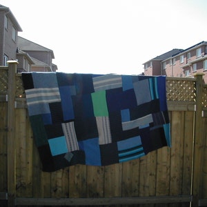 May include: A blue and green patchwork quilt hanging on a wooden fence. The quilt is made of different shades of blue and green fabric, and it has a variety of patterns.