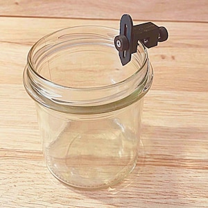 May include: A clear glass jar with a black plastic clamp attached to the rim.