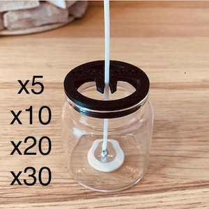 May include: A clear glass jar with a black lid and a white stirring mechanism. The text "x5", "x10", "x20", and "x30" are printed on the left side of the jar. The jar is sitting on a wooden surface.