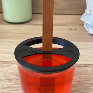 Könnte beinhalten: Ein klares Glasgefäß mit einem schwarzen Deckel und den Worten "idee Creation 3D" auf dem Deckel. Das Gefäß ist mit einer roten Flüssigkeit gefüllt und ein Holzstab ist durch den Deckel in die Flüssigkeit gesteckt.