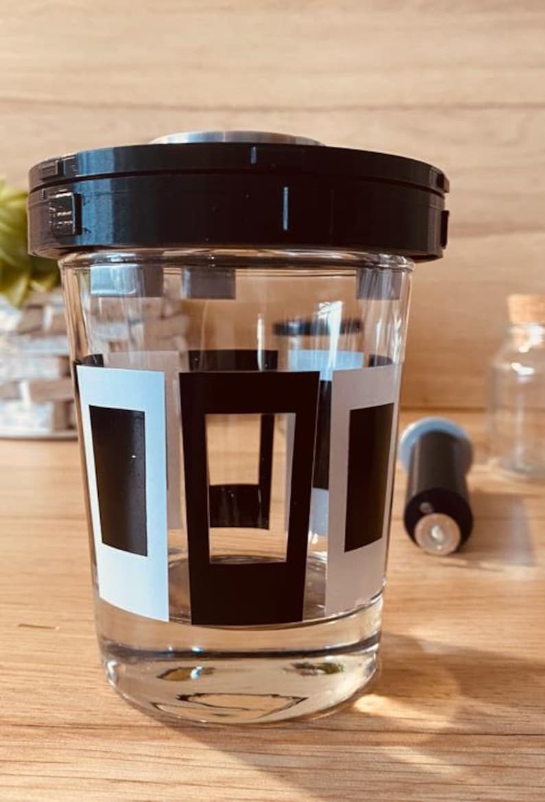 May include: A clear glass jar with a black lid and a black and white geometric design. The jar is filled with a clear liquid.
