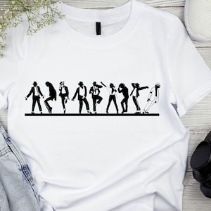 May include: White t-shirt featuring a black silhouette of a group of people in various dance poses. The design is a line of figures in motion, with a focus on dance. The shirt is displayed on a wooden surface, with jeans, headphones, and shoes in the background.