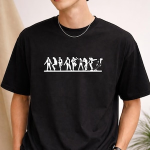 May include: Black t-shirt featuring a white graphic of stylized figures in various poses. The design is centered on the chest. The shirt has short sleeves and a crew neck. The model is wearing a silver chain.