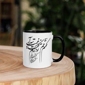 Puede incluir: Taza de cerámica blanca con asa y borde negros, con elegante caligrafía negra. La taza está colocada sobre una superficie de madera, con un fondo verde borroso.