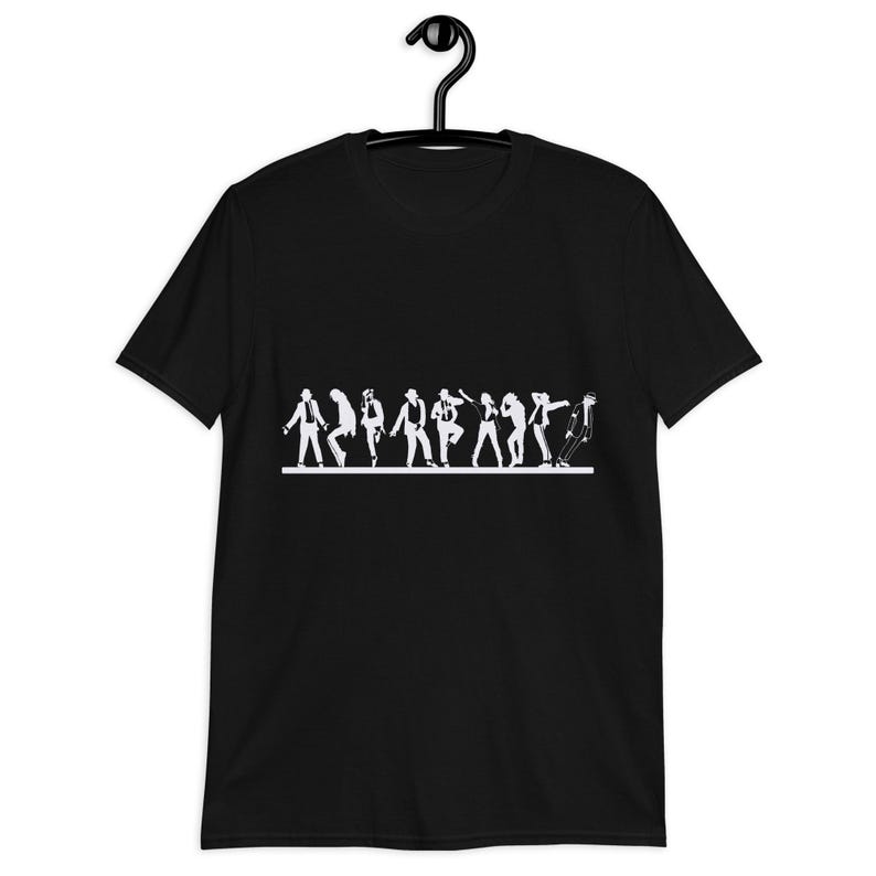 May include: Black t-shirt featuring a white silhouette of a line of dancers in various poses. The design includes figures in hats and suits, with one figure leaning forward. The shirt is hanging on a black hanger.