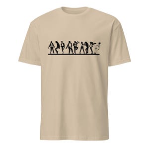 May include: A tan t-shirt featuring a black silhouette of a line of people in various dance poses. The figures are depicted in a stylized, minimalist design, creating a dynamic and rhythmic visual effect. The shirt is made of a soft, comfortable material.