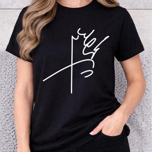 Puede incluir: Camiseta negra con un diseño abstracto blanco, posiblemente una corona o un motivo floral. La camiseta tiene cuello redondo y se combina con vaqueros negros. El diseño es minimalista y moderno.
