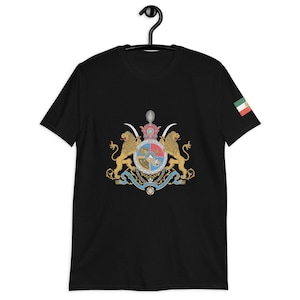 Puede incluir: Camiseta negra con un emblema detallado con dos leones dorados, una corona y un escudo. El emblema está centrado, con una pequeña bandera en la manga derecha. La camiseta está colgada en una percha negra.