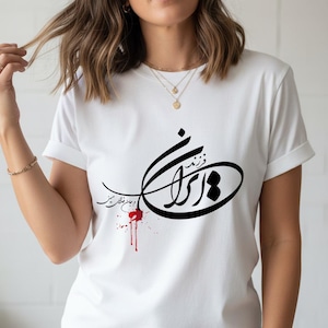 Puede incluir: Camiseta blanca con un diseño de caligrafía negra y un efecto de salpicadura roja. El diseño incluye una forma ovalada con texto en el interior y escritura adicional arriba y abajo. La camiseta tiene mangas cortas.