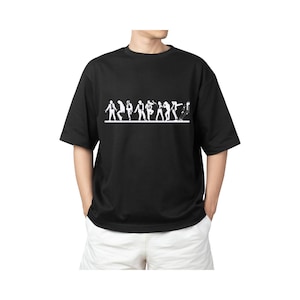 May include: Black t-shirt with a white graphic of stylized figures in various poses, possibly dancing or performing. The shirt has short sleeves and a crew neck. The model is wearing white shorts.