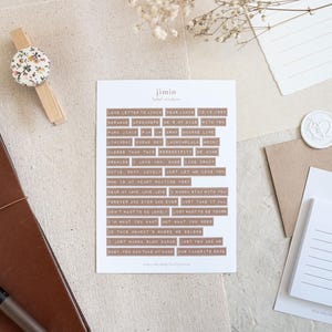 May include: A stationery flat lay featuring a brown leather journal, a pen, and a sheet of stickers with text. A wooden clothespin with a floral design and a small notepad with a dog illustration are also present.