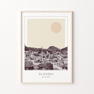 May include: A minimalist black and white illustration of the city of Plovdiv, Bulgaria, with a beige background and a peach-colored circle in the upper right corner. The text "Plovdiv" and "Bulgaria" is printed in maroon below the illustration.