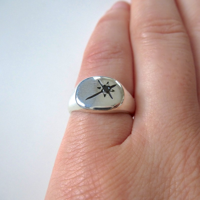 May include: A silver signet ring featuring a black star design. The star has a small black gemstone at its centre.