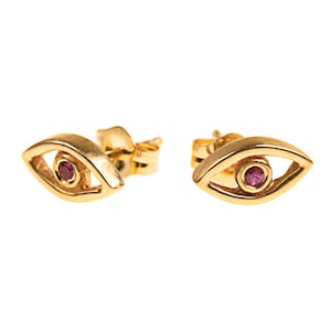 May include: A pair of gold earrings with a small, pink gemstone in the center of each earring. The earrings are shaped like an eye.