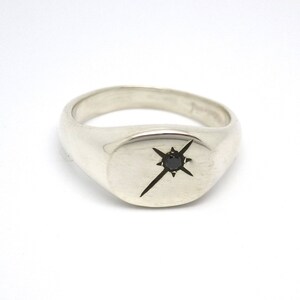May include: A silver signet ring featuring a black diamond set in a starburst design.