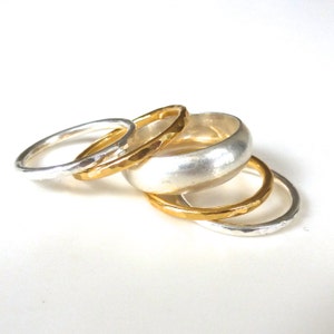 May include: A set of five silver and gold rings. The rings are stacked on top of each other. The rings are all different sizes and widths. The rings are made of metal and have a smooth finish.
