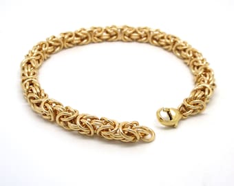 Op de afbeelding: Een gouden kettingarmband met een geweven ontwerp. De armband heeft een sluiting.