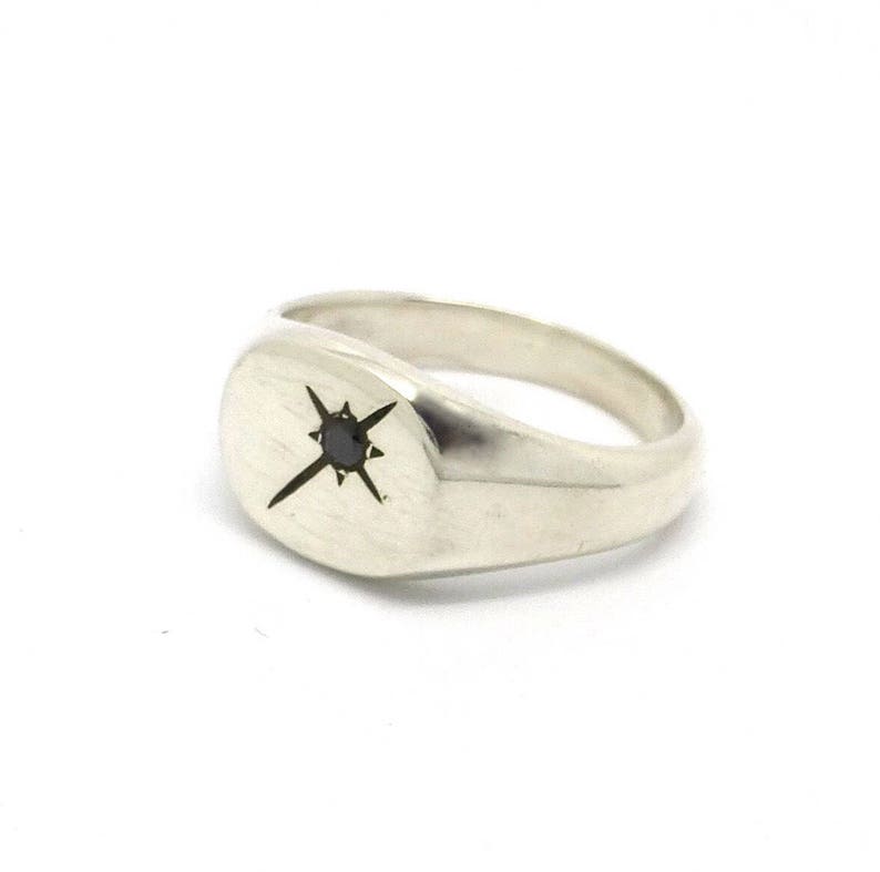 May include: A silver signet ring featuring a black diamond set in a starburst design.