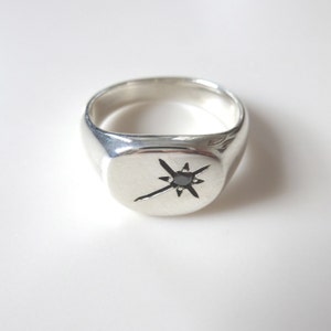 May include: A silver signet ring featuring a black gemstone set in a star design.