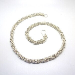 May include: A silver chain necklace with a box chain design. The necklace is made of interlocking metal rings.