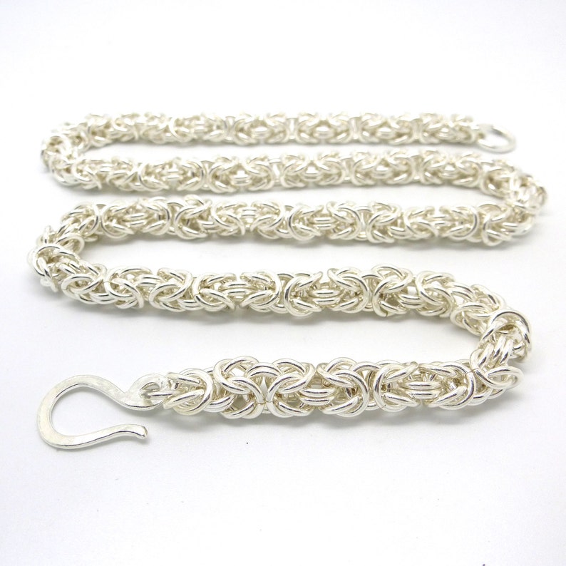 May include: A silver chain necklace with a hook clasp. The chain is made of multiple interwoven links, creating a complex and intricate design.