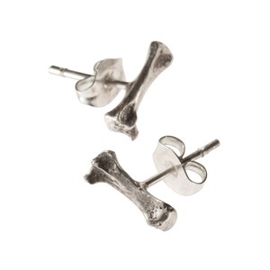 Könnte beinhalten: Ein Paar silberne Ohrstecker in Knochenform. Die Ohrringe sind aus Metall und haben ein schlichtes Design.