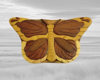 Puede incluir: Una escultura de mariposa de madera con un diseño detallado. La mariposa tiene alas marrones con detalles amarillos y un cuerpo amarillo. La escultura está hecha de diferentes tonos de madera y tiene una apariencia natural y artesanal.