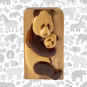 May include: A wooden panda bear sculpture with a light brown body and dark brown accents, hugging a smaller panda. The sculpture is mounted on a rectangular wooden plaque. The panda's fur is a light tan color.