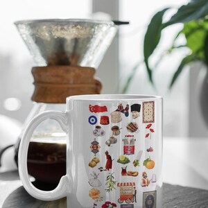 May include: White ceramic mug decorated with colorful illustrations of Turkish cultural symbols. The mug features images of the Turkish flag, food, and landmarks. A coffee pour-over setup is in the background.