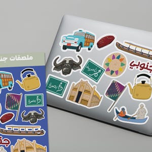 May include: A collection of colorful stickers featuring illustrations of a vintage bus, a teapot, a buffalo, a boat, a woven plate, a flag, and other cultural symbols. The stickers are on a laptop and a card.