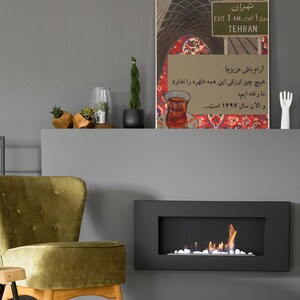 May include: An interior shot featuring a framed artwork with Persian text and a Tehran sign. A green velvet chair and a small wooden table are in the foreground. A modern fireplace with flames is on the wall.