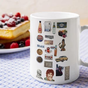 May include: White ceramic mug decorated with various Iranian cultural icons and the word "IRAN". The mug is set on a blue and white checkered cloth, with a plate of French toast and berries in the background.