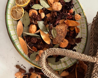 May include: An oval, vintage-style tray with a green and white checkered pattern, filled with dried botanicals. The arrangement includes dried orange slices, bay leaves, and various brown and tan dried flowers and seed pods. A woven basket handle is visible.